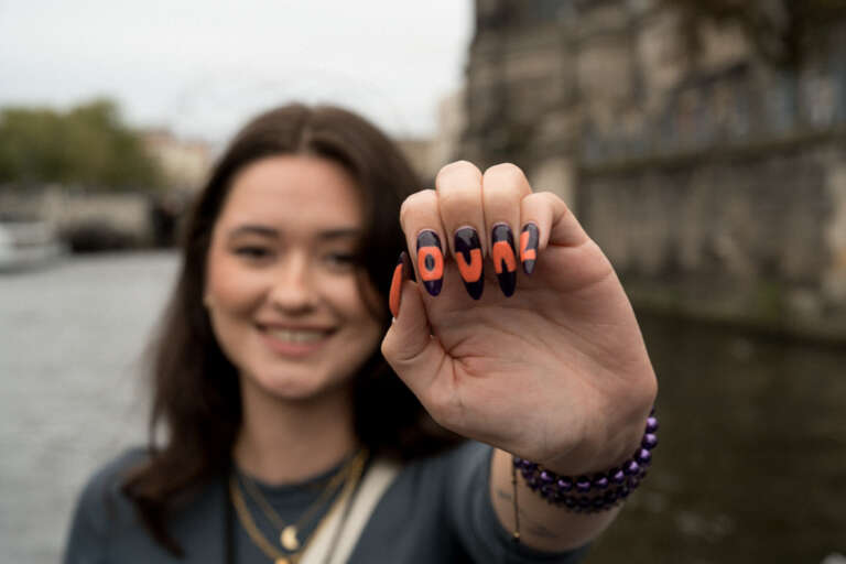 Jeune collaboratrice souriante affichant fièrement une manucure avec les lettres OVAL, symbole d’appartenance à l’agence